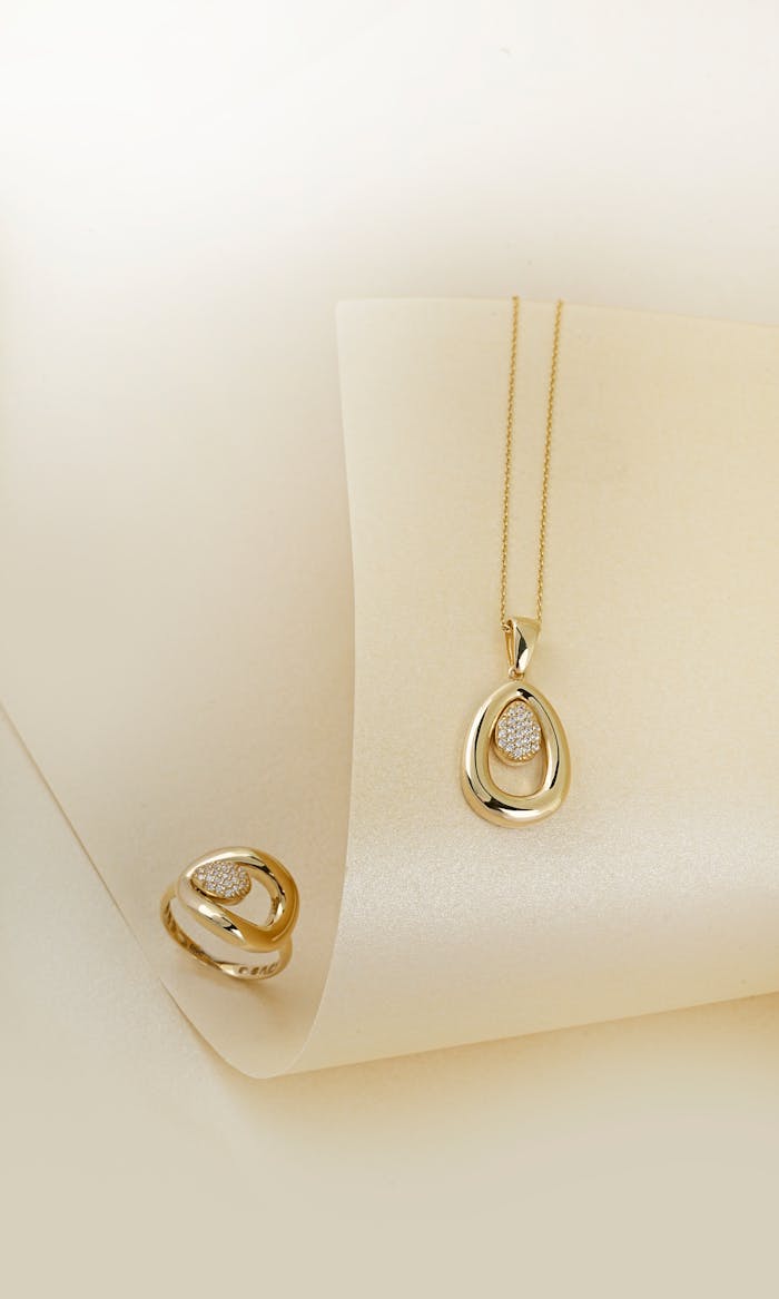 gallery-6 Luxurious gold ring and necklace set with diamonds displayed on a soft cream backdrop.